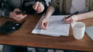 زوجان يراجعان أوراقًا مالية وآلة حاسبة على طاولة خشبية لوضع خطة سداد الديون