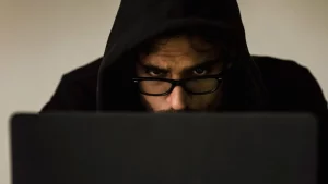 شخص بقلنسوة أمام حاسوب محمول في الظلام يرمز إلى مخاطر الاحتيال والتصيد الإلكتروني