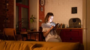 امرأة تستخدم هاتفها في مساء دافئ داخل بيت مريح ترمز إلى إدارة حساب تطبيق التعارف وحذف البيانات
